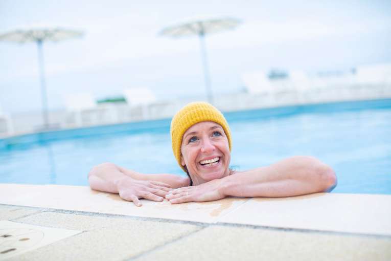 Lady smiling in the outdoor pool with a beanie on, cold water swimming