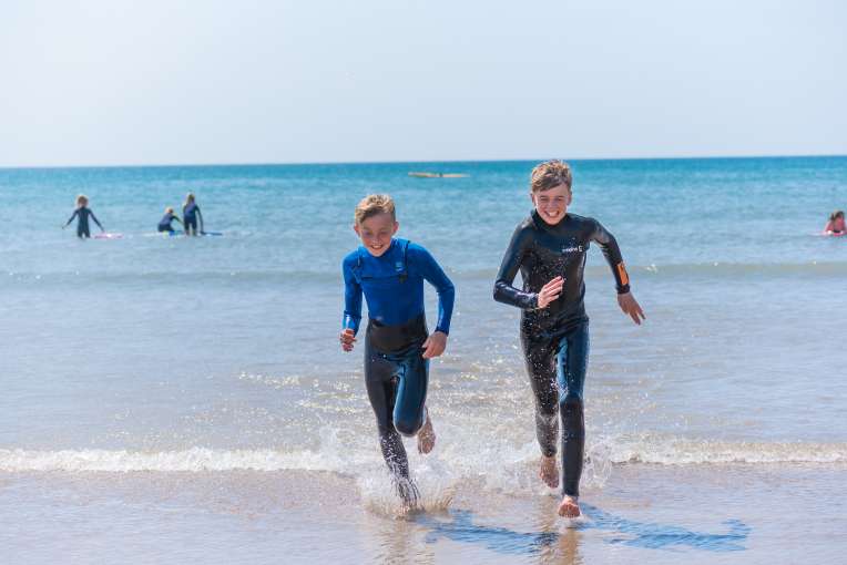 Two friends running out of the sea in their wetsuits 