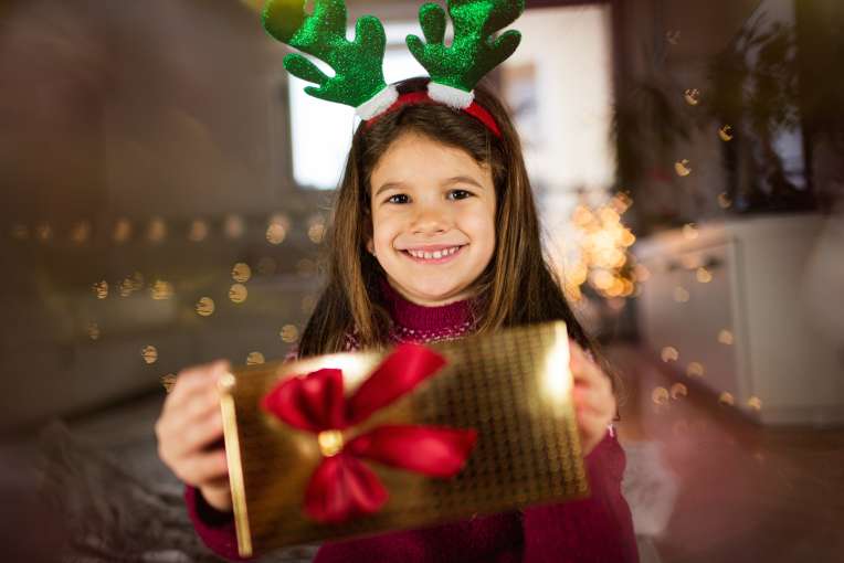 Young girl holding a Christmas present wearing Rudolf antlers