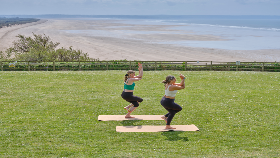 Two ladies doing a yoga pose on the lawn with a view of the beach at Saunton Sands Hotel