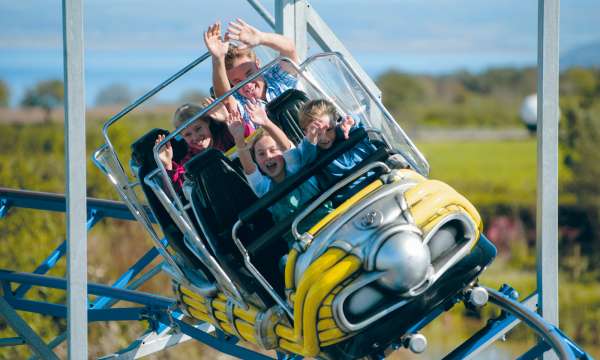 Kids on a yellow rollercoaster at The Milky Way Adventure Park with their hands up 