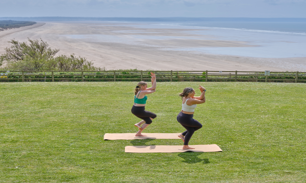 Two ladies doing a yoga pose on the lawn with a view of the beach at Saunton Sands Hotel