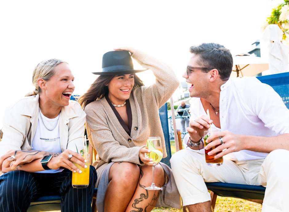 Three friends sat on the deck chairs with cocktails laughing