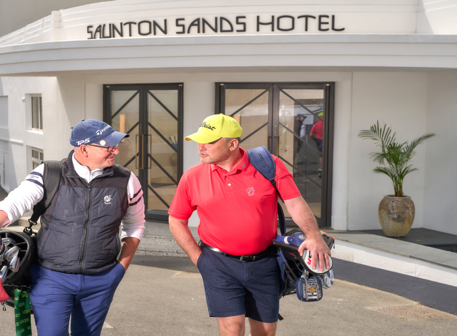 2 men walking at the front of the hotel with golf bags 