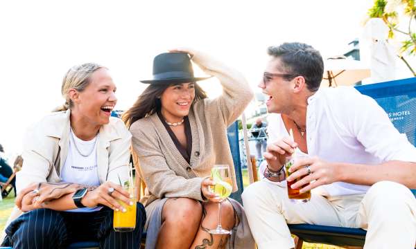 Three friends sat on the deck chairs with cocktails laughing
