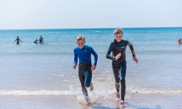 Two friends running out of the sea in their wetsuits